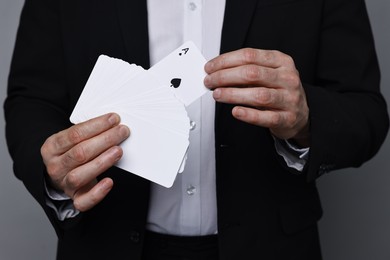 Photo of Illusionist with playing cards on grey background, closeup