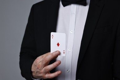 Photo of Illusionist with playing card on grey background, closeup