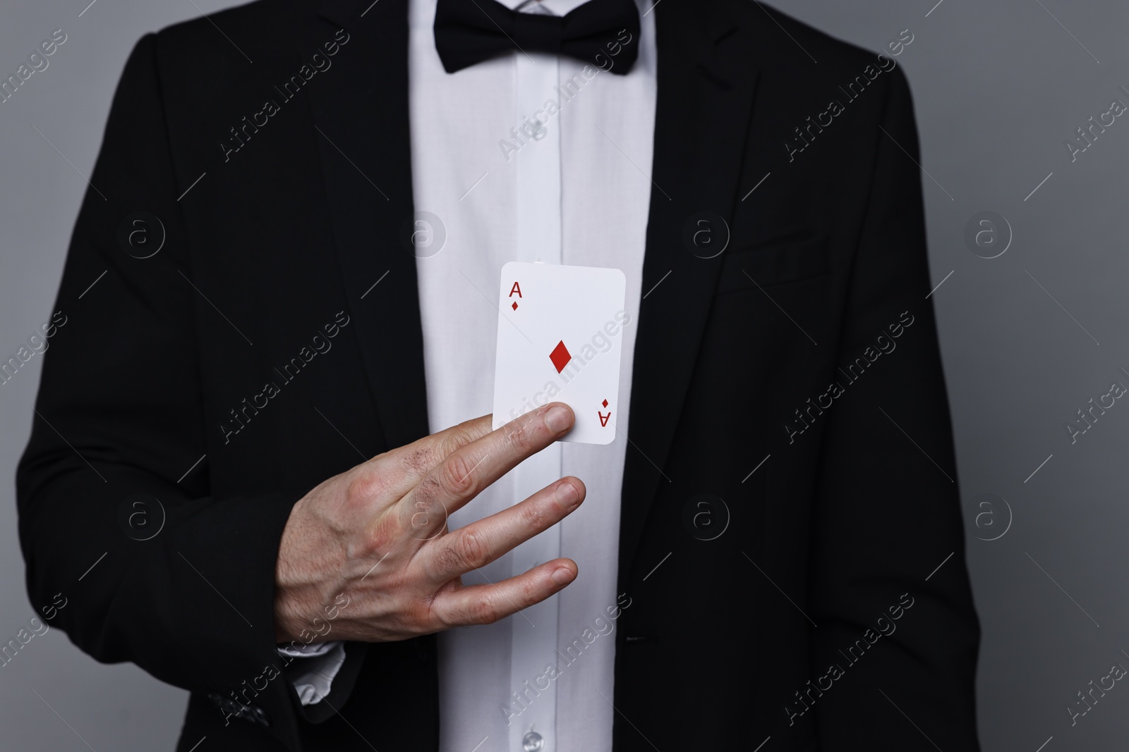 Photo of Illusionist hiding playing card behind jacket lapel on grey background, closeup