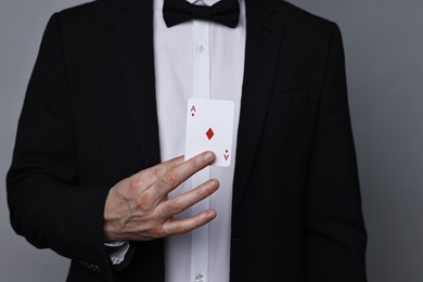 Photo of Illusionist hiding playing card behind jacket lapel on grey background, closeup