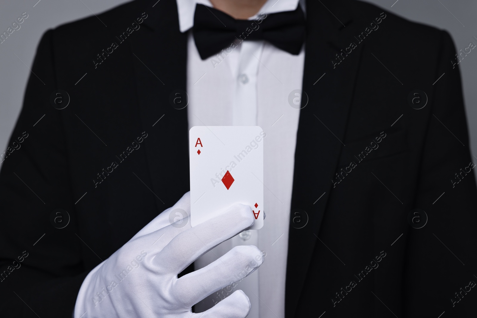 Photo of Illusionist with playing card on grey background, closeup