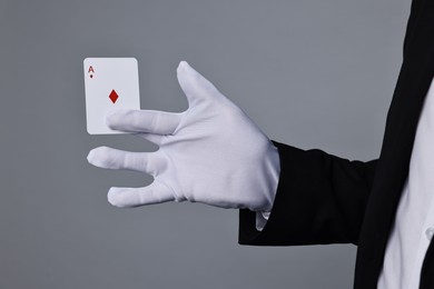 Photo of Illusionist with playing card on grey background, closeup