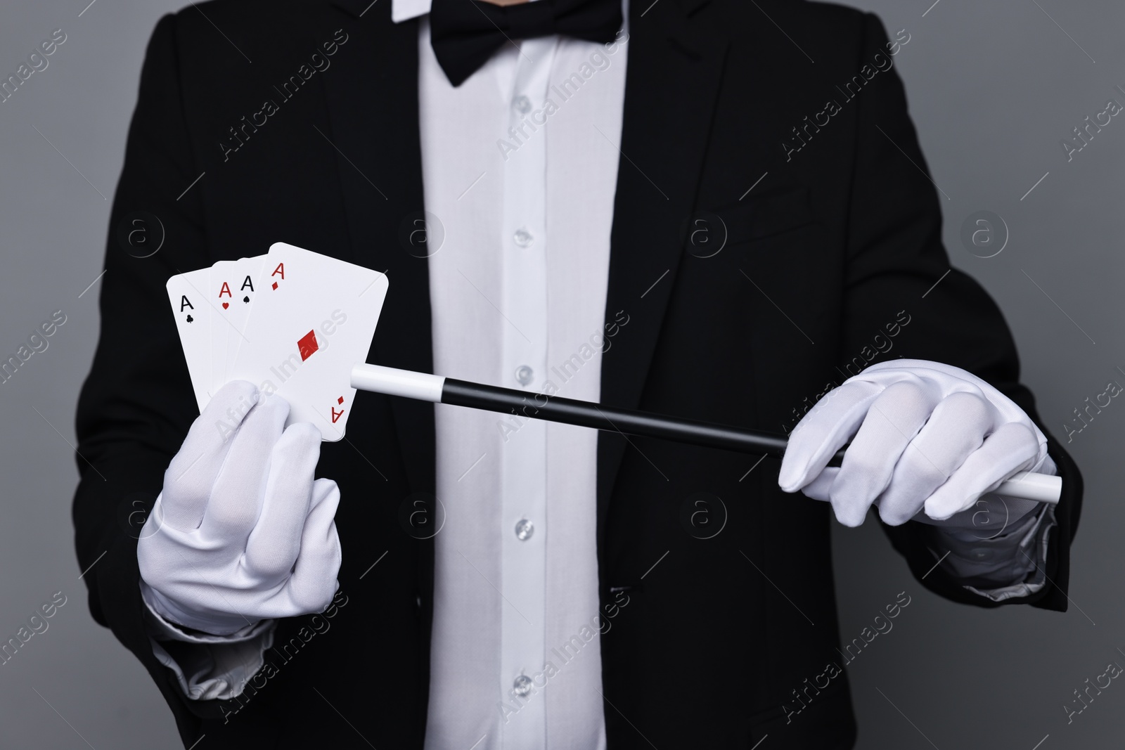 Photo of Illusionist pointing magic wand on playing cards against grey background, closeup