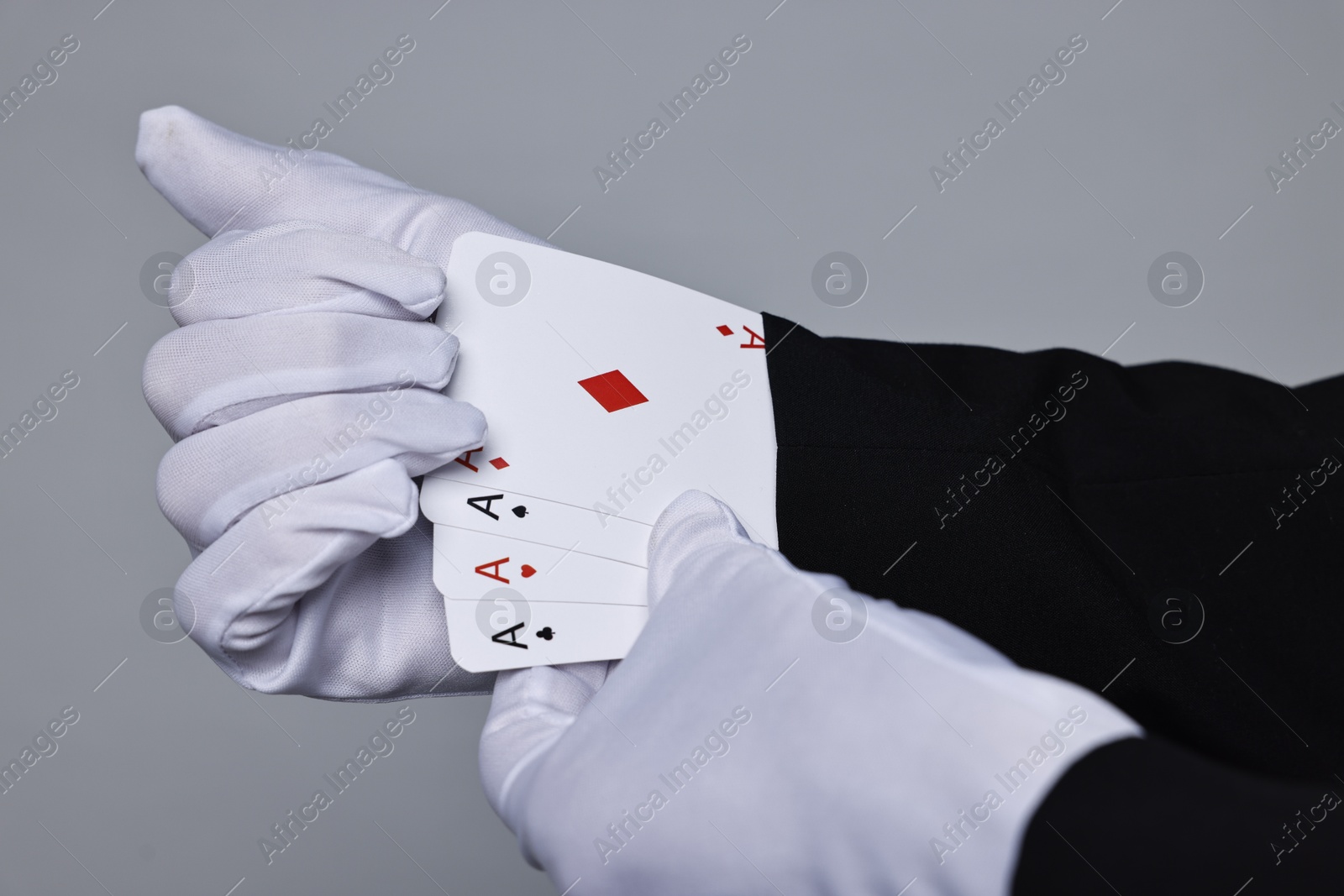 Photo of Illusionist taking playing cards out of sleeve on grey background, closeup