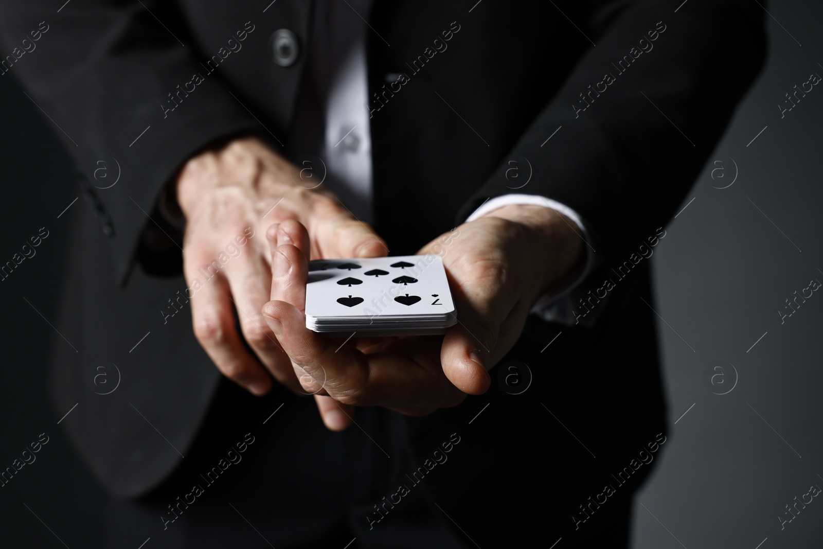 Photo of Illusionist with playing cards on grey background, closeup