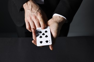 Photo of Illusionist with playing cards at black table, closeup