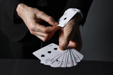 Photo of Illusionist hiding one playing card up his sleeve while showing deck at black table, closeup