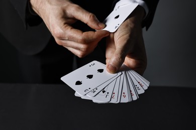 Photo of Illusionist hiding one playing card up his sleeve while showing deck at black table, closeup