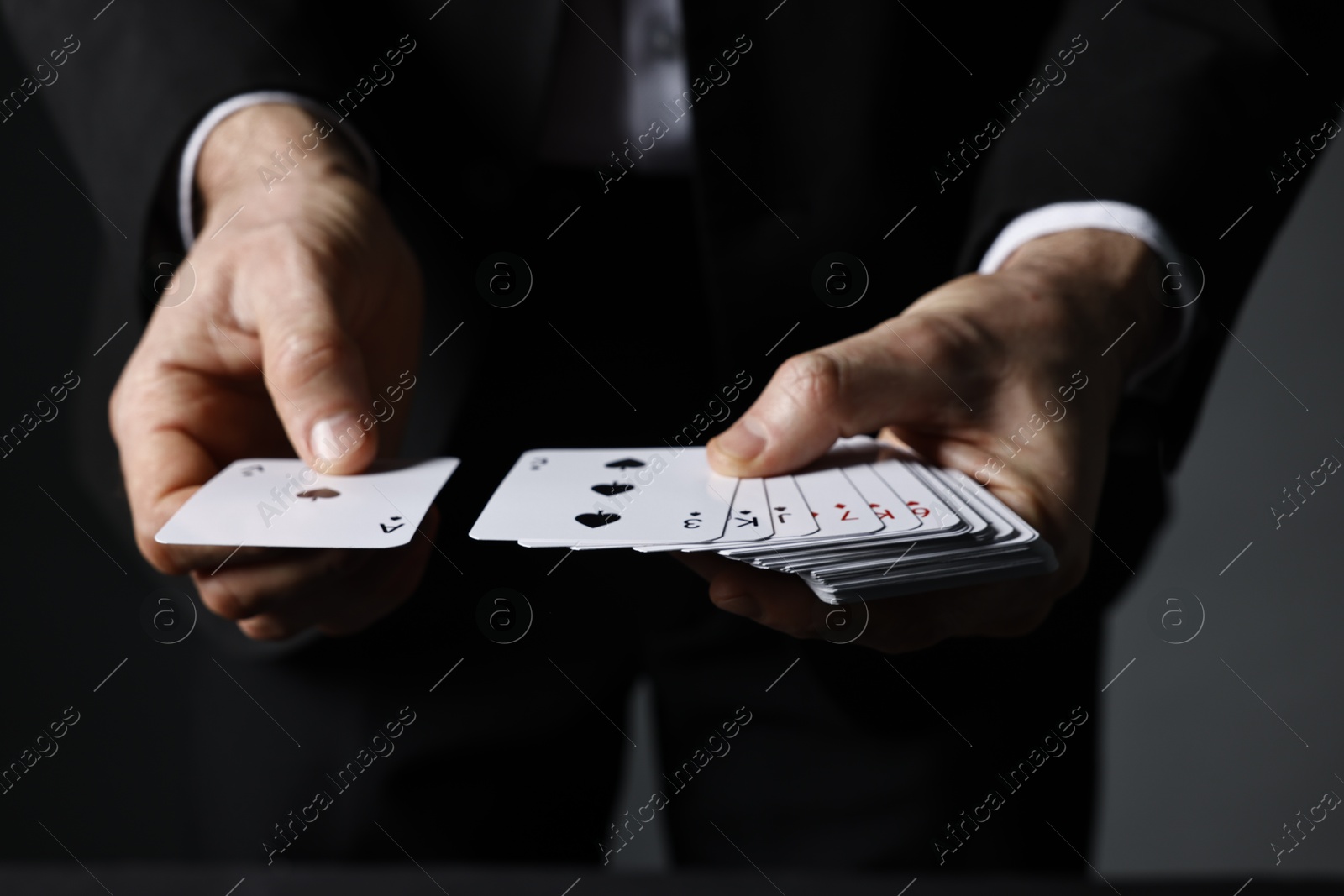 Photo of Illusionist shuffling playing cards on grey background, closeup