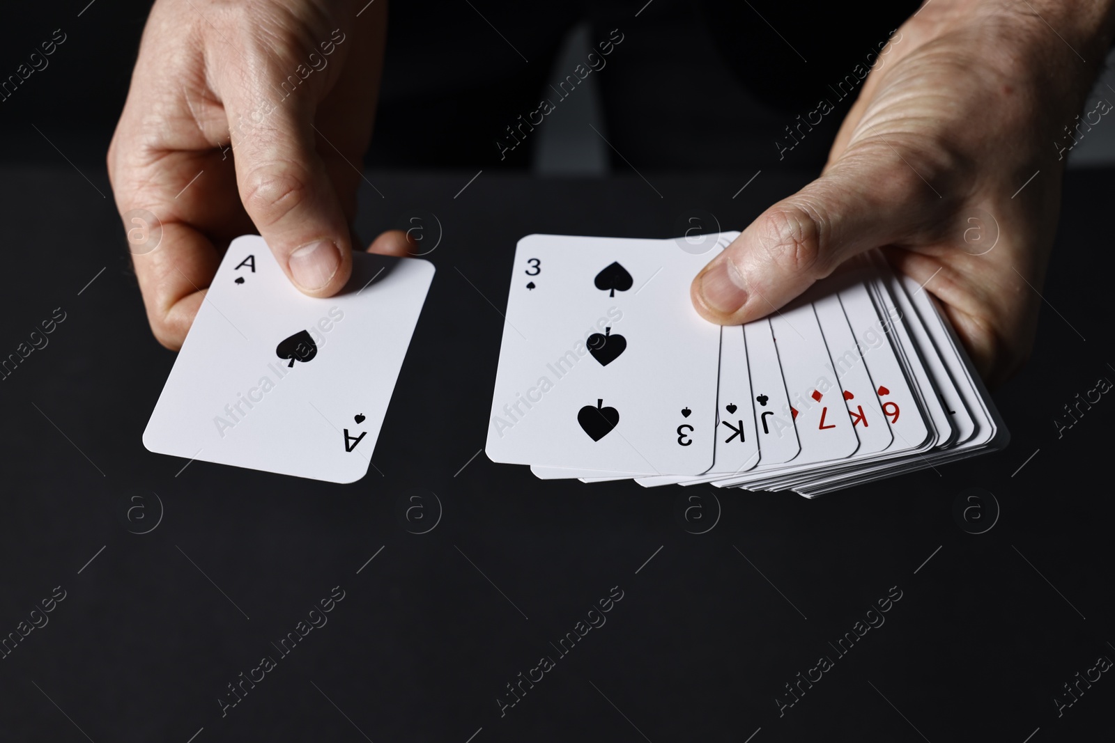 Photo of Illusionist shuffling playing cards on black background, closeup