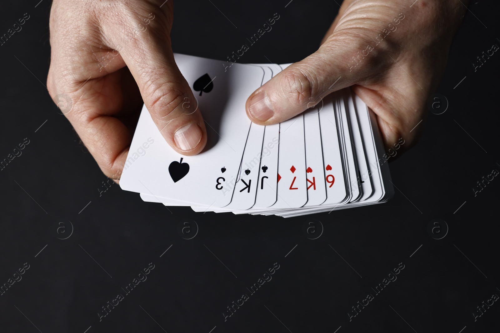 Photo of Illusionist shuffling playing cards on black background, closeup