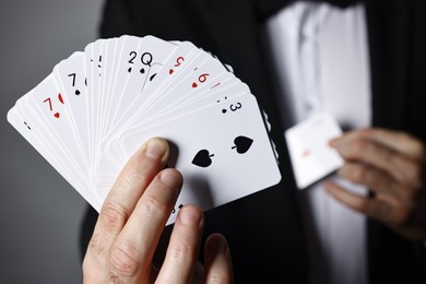 Photo of Illusionist hiding one playing card behind jacket lapel while showing deck on grey background, selective focus