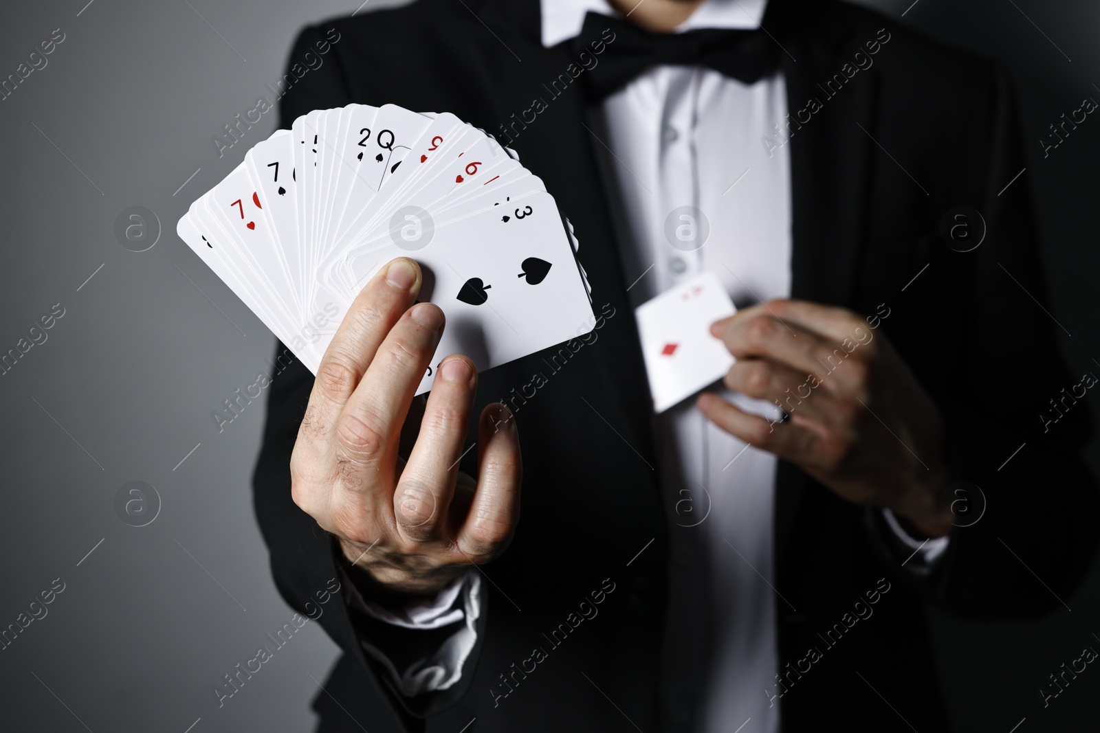 Photo of Illusionist hiding one playing card behind jacket lapel while showing deck on grey background, selective focus