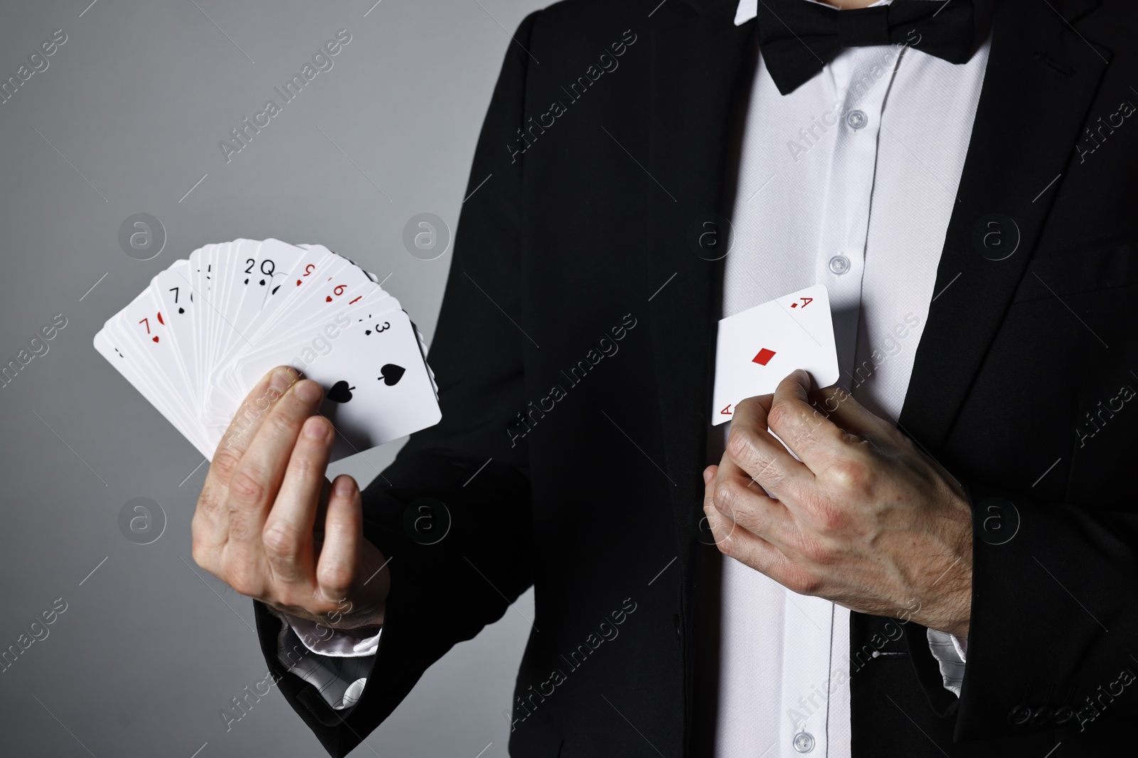 Photo of Illusionist hiding one playing card behind jacket lapel while showing deck on grey background, closeup