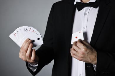 Photo of Illusionist hiding one playing card behind jacket lapel while showing deck on grey background, closeup