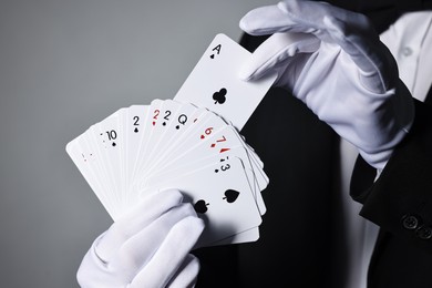 Photo of Illusionist with playing cards on grey background, closeup