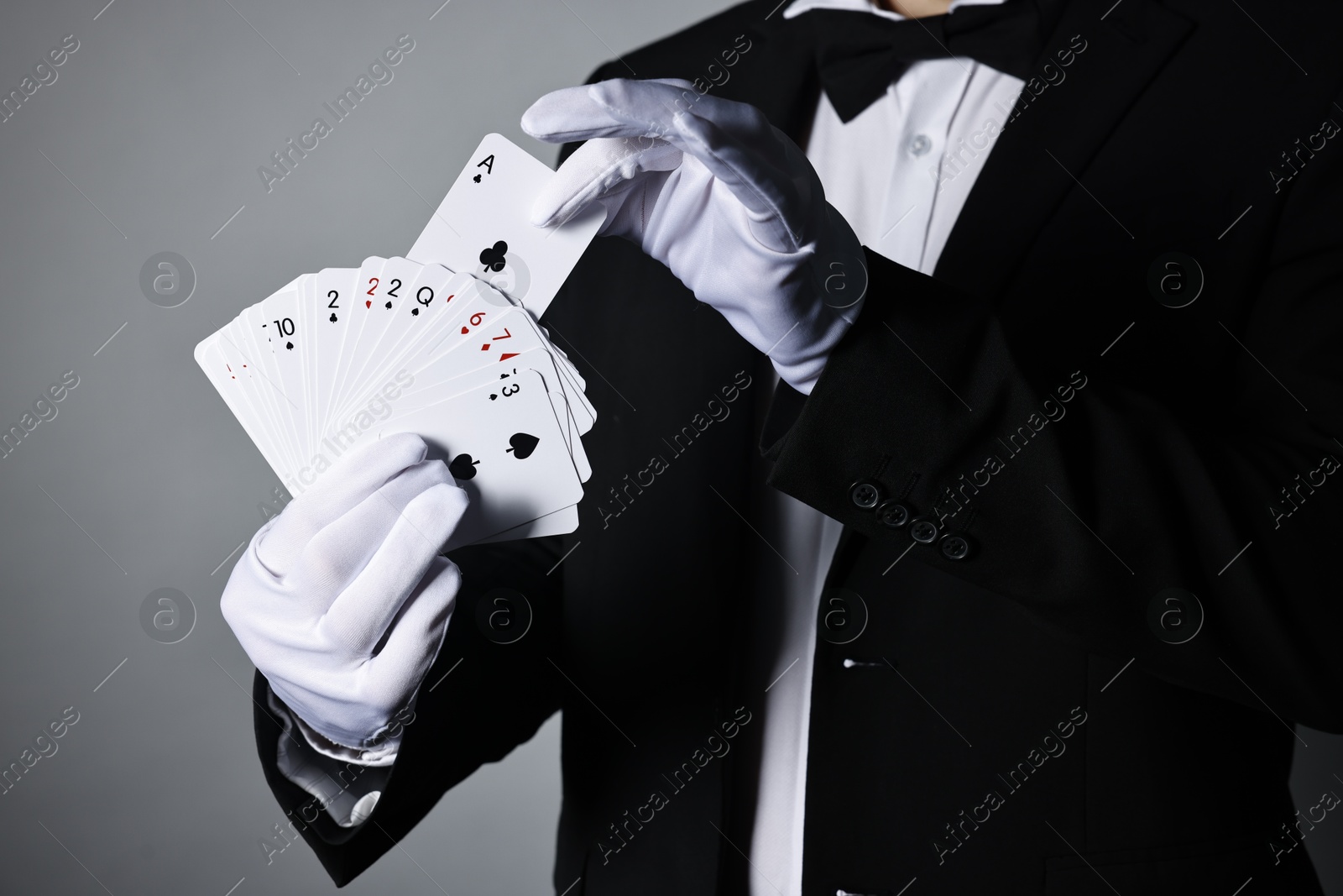 Photo of Illusionist with playing cards on grey background, closeup