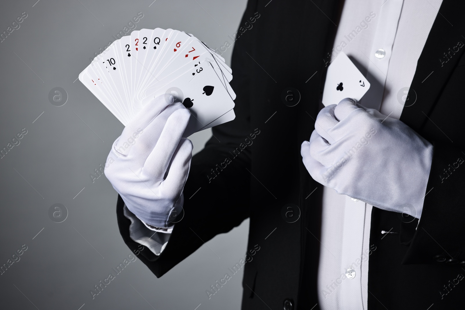 Photo of Illusionist hiding one playing card behind jacket lapel while showing deck on grey background, closeup