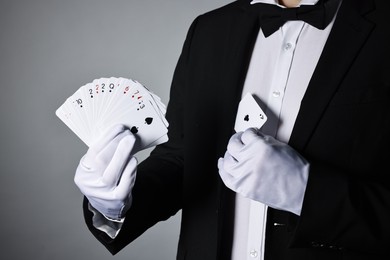 Photo of Illusionist hiding one playing card behind jacket lapel while showing deck on grey background, closeup