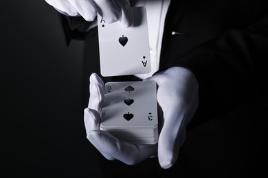 Photo of Illusionist shuffling playing cards on black background, closeup