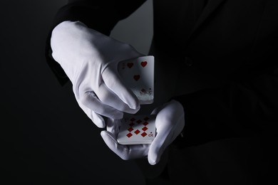 Photo of Illusionist shuffling playing cards on black background, closeup