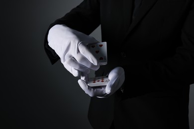 Photo of Illusionist shuffling playing cards on black background, closeup