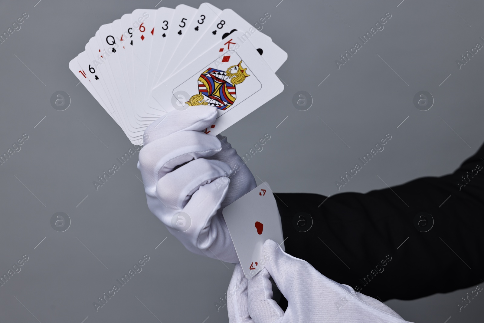 Photo of Illusionist hiding one playing card up his sleeve while showing deck on grey background, closeup