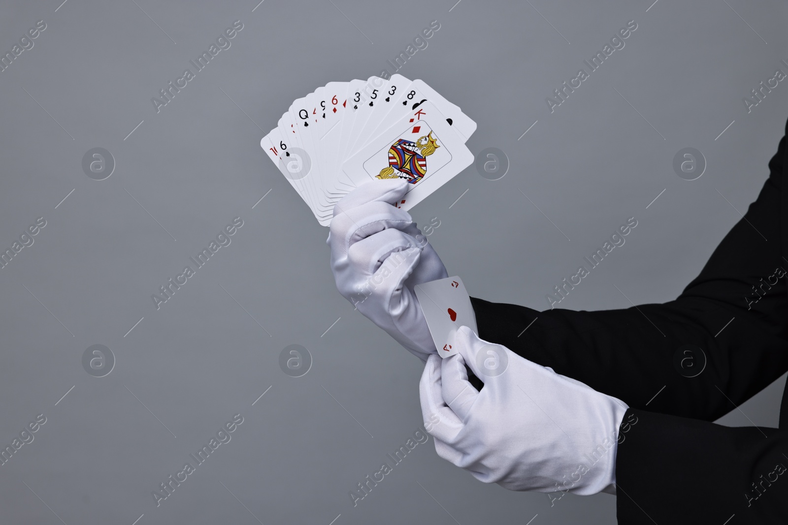 Photo of Illusionist hiding one playing card up his sleeve while showing deck on grey background, closeup