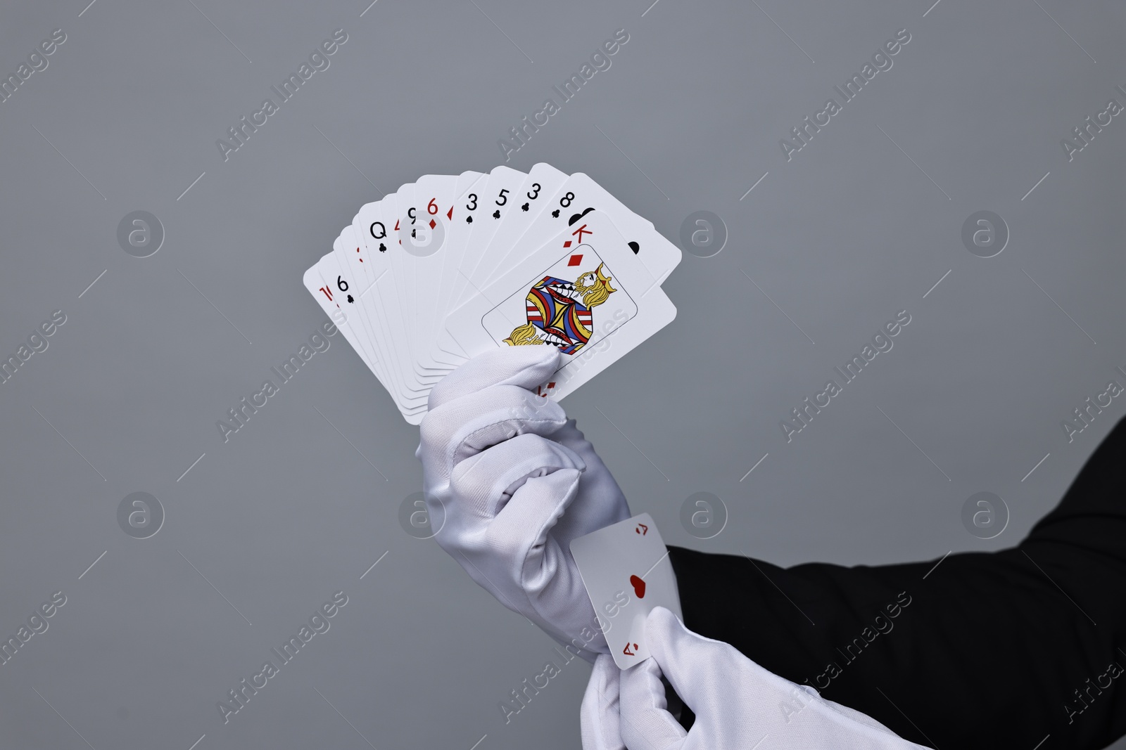 Photo of Illusionist hiding one playing card up his sleeve while showing deck on grey background, closeup