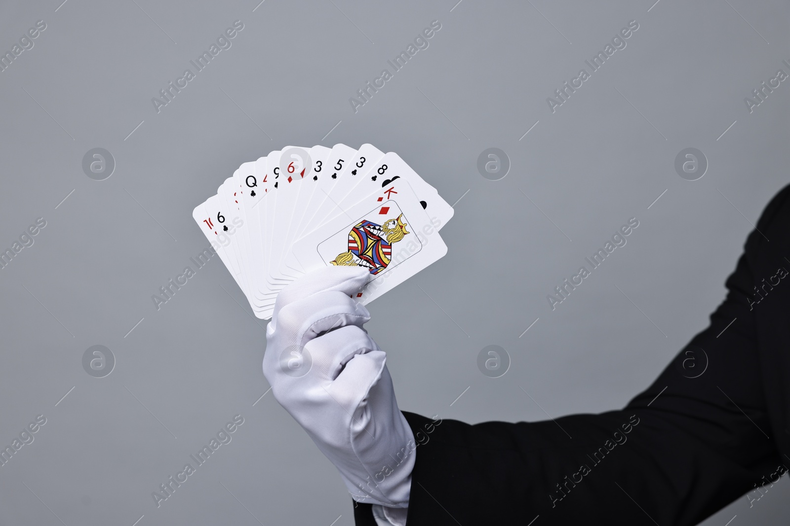 Photo of Illusionist with playing cards on grey background, closeup