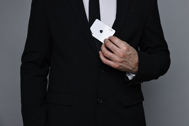 Photo of Illusionist hiding playing card behind jacket lapel on grey background, closeup