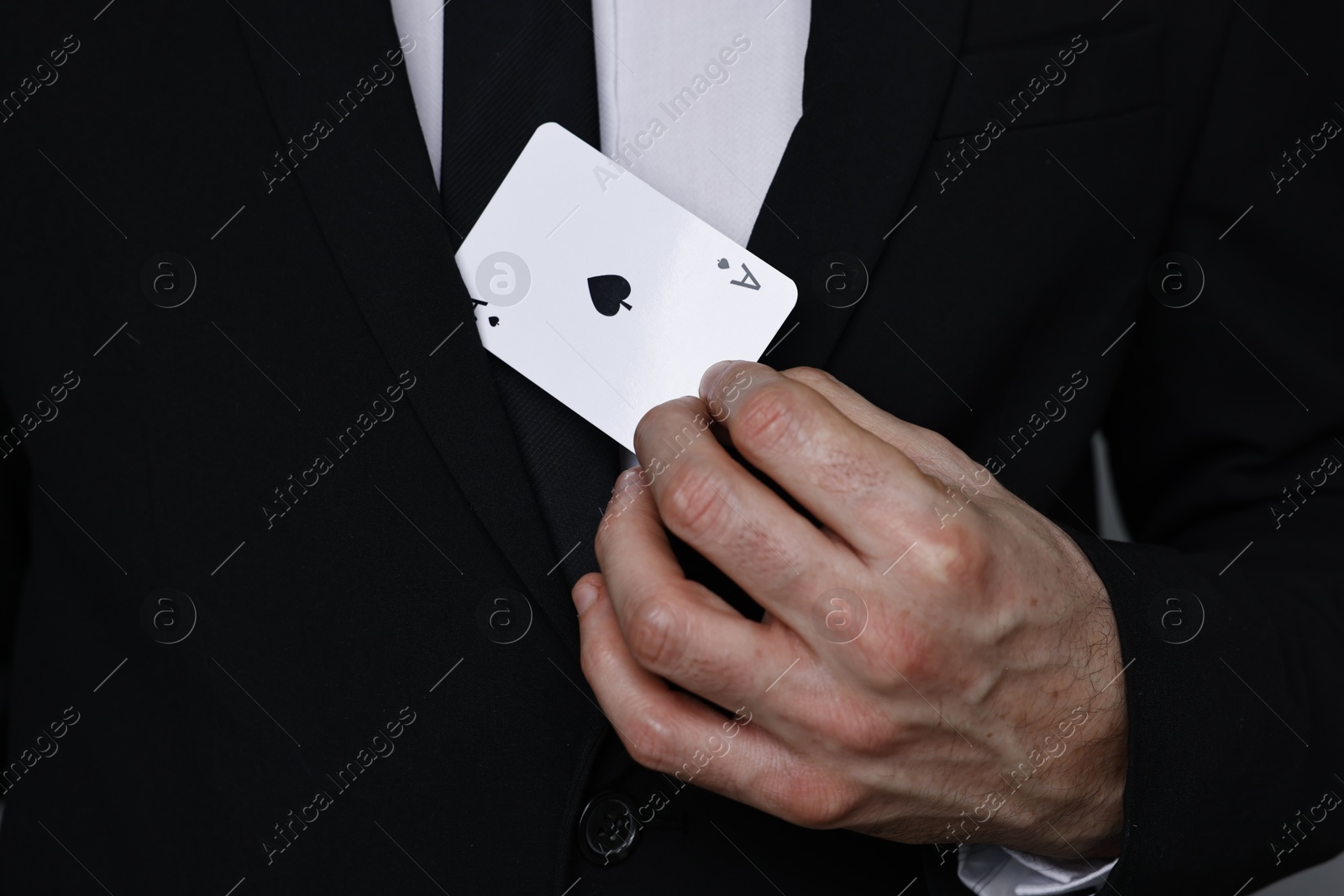 Photo of Illusionist hiding playing card behind jacket lapel on grey background, closeup