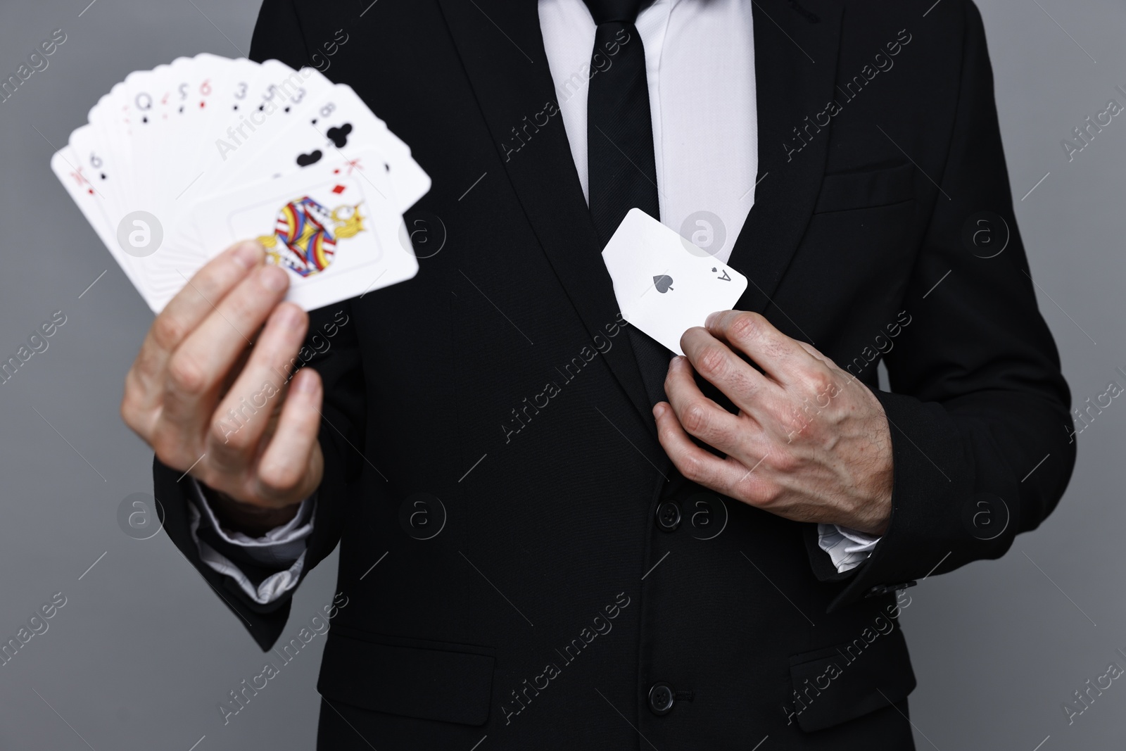 Photo of Illusionist hiding one playing card behind jacket lapel while showing deck on grey background, closeup