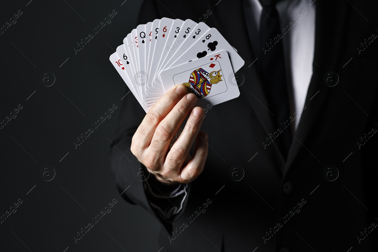 Photo of Illusionist with playing cards on black background, closeup