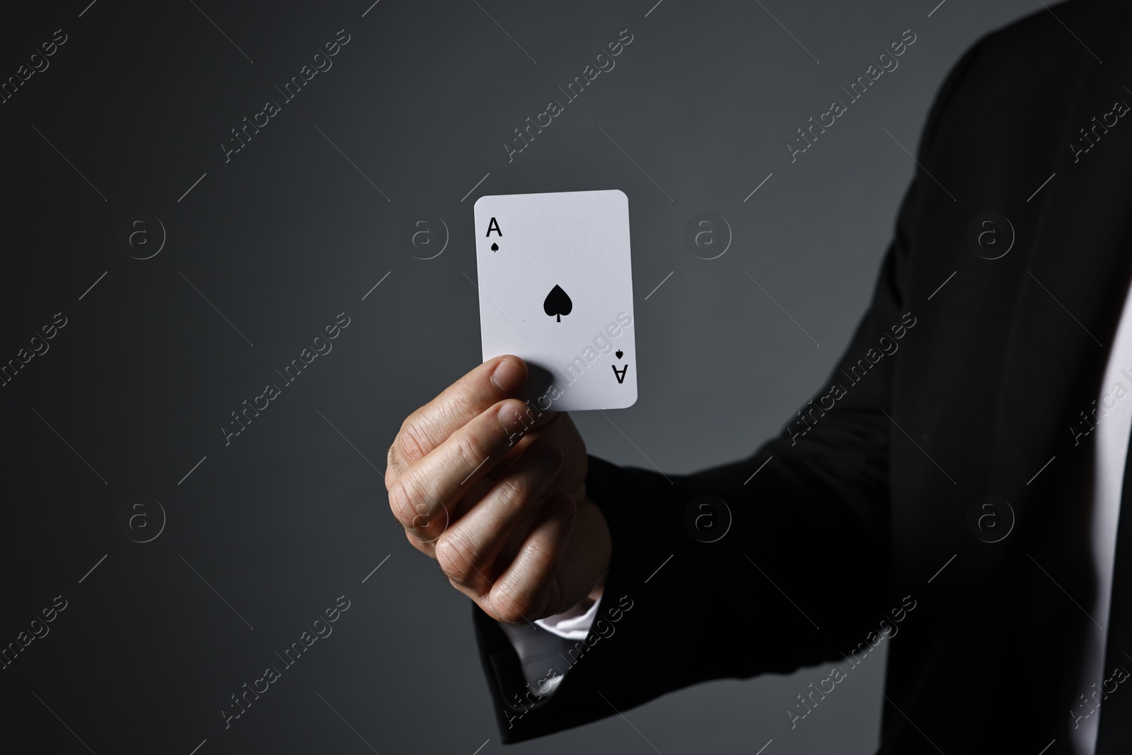 Photo of Illusionist with playing card on grey background, closeup