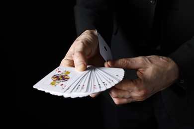 Photo of Illusionist hiding one playing card up his sleeve while showing deck on black background, closeup