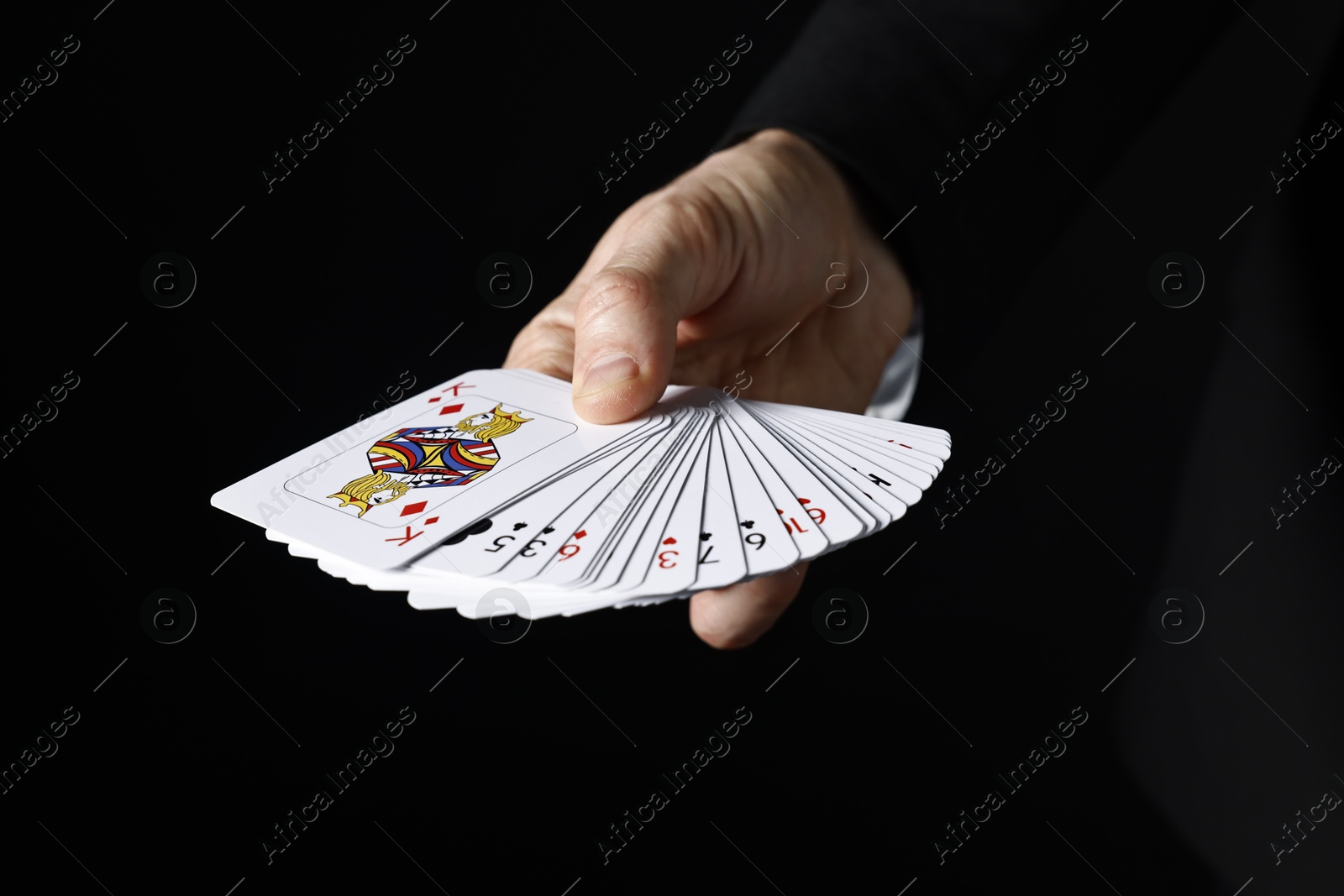 Photo of Illusionist with playing cards on black background, closeup