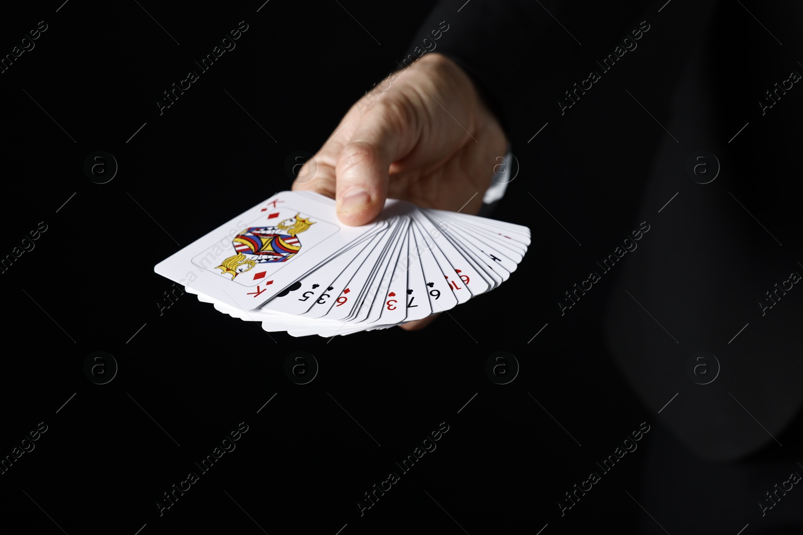 Photo of Illusionist with playing cards on black background, closeup