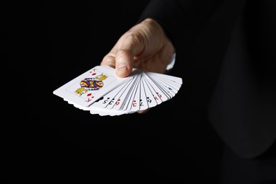 Photo of Illusionist with playing cards on black background, closeup