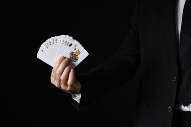 Photo of Illusionist with playing cards on black background, closeup