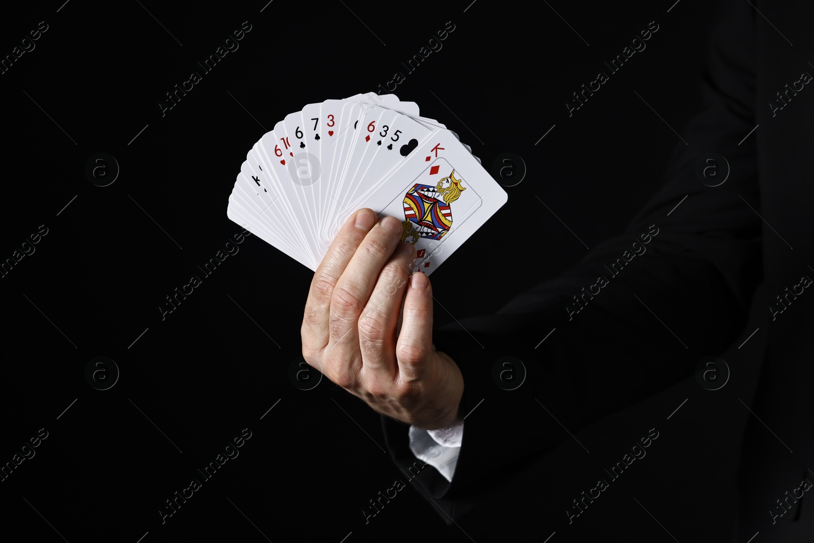 Photo of Illusionist with playing cards on black background, closeup