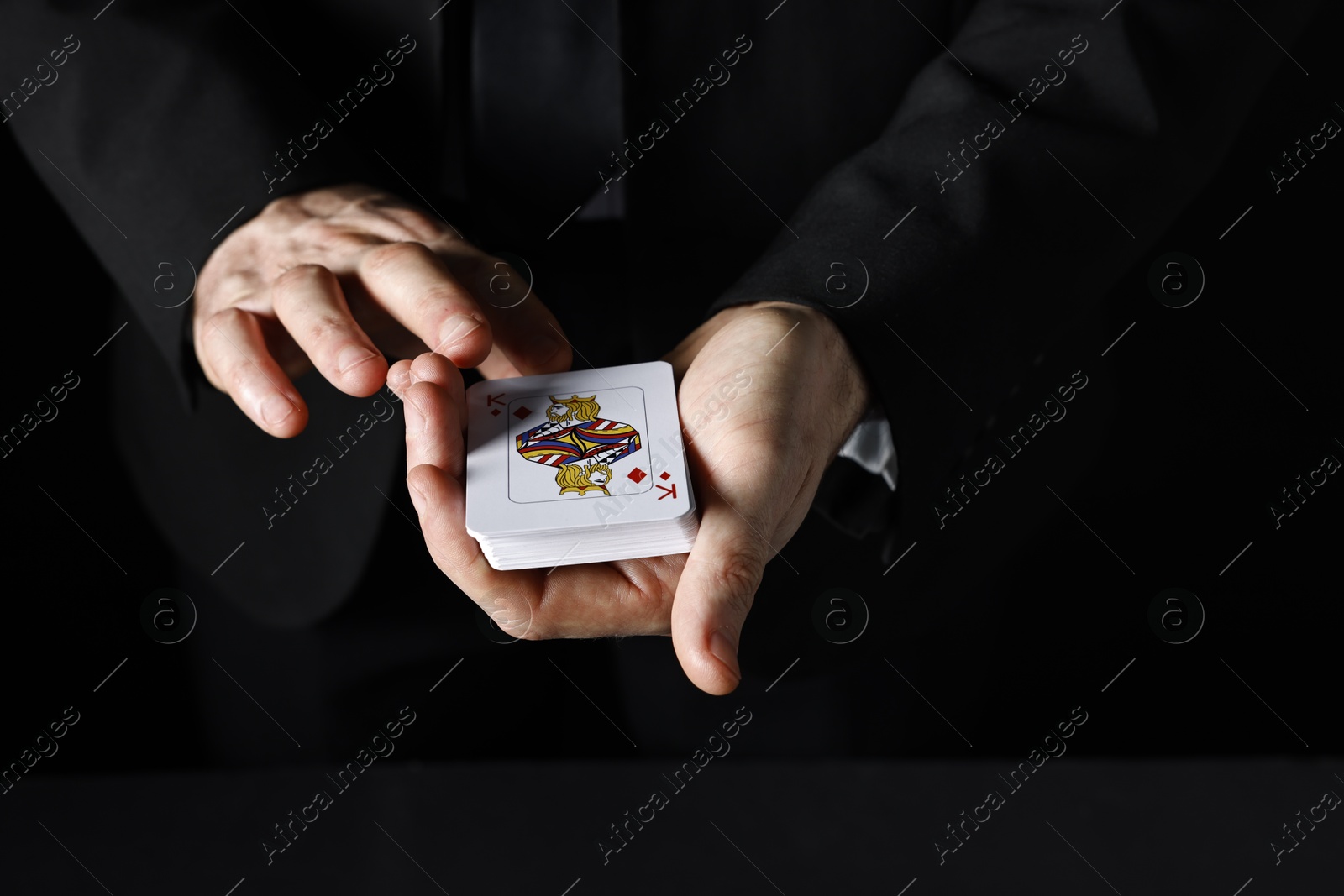 Photo of Illusionist with playing cards on black background, closeup