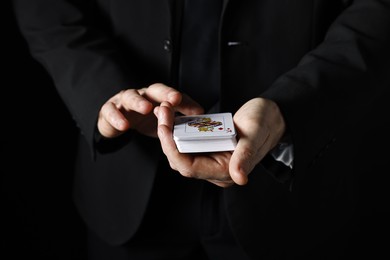 Illusionist with playing cards on black background, closeup