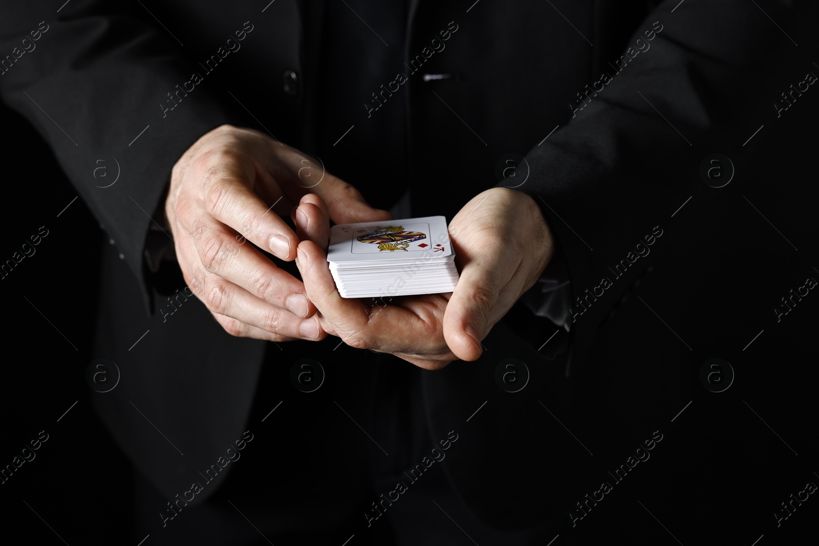 Photo of Illusionist with playing cards on black background, closeup