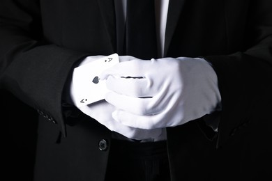 Photo of Illusionist taking playing card out of sleeve on black background, closeup