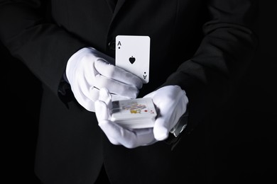 Photo of Illusionist with playing cards on black background, closeup