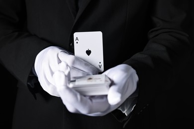 Photo of Illusionist with playing cards on black background, closeup