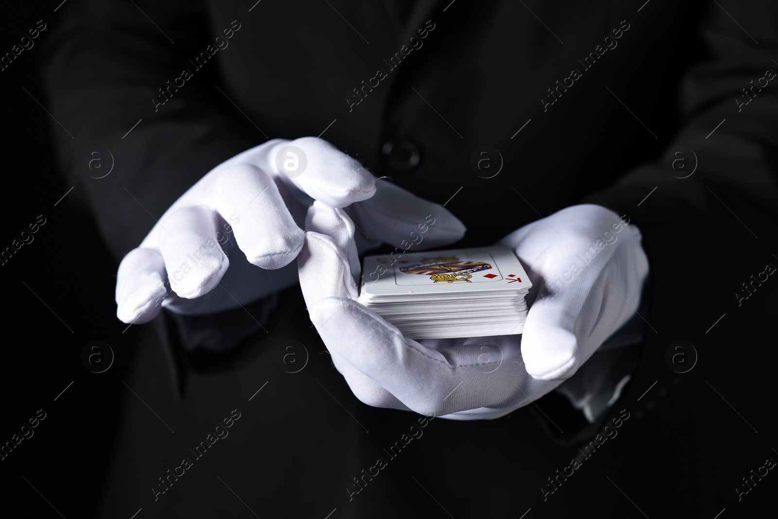 Photo of Illusionist with playing cards on black background, closeup