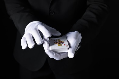 Photo of Illusionist with playing cards on black background, closeup