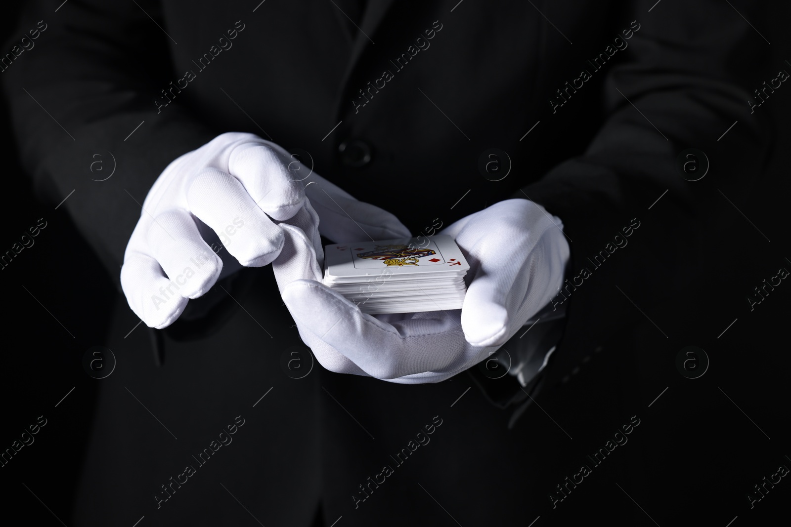 Photo of Illusionist with playing cards on black background, closeup